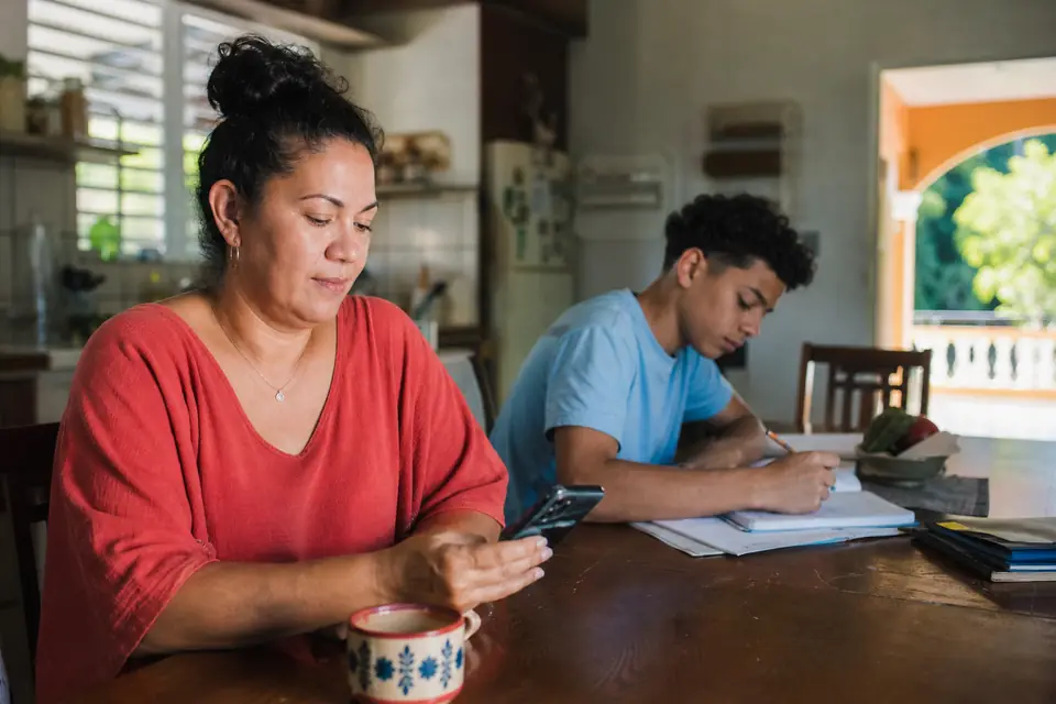 Madre revisa su cuenta bancaria en el celular junto a su hijo en la cocina