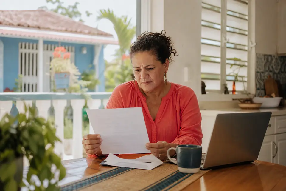 Mujer en la mesa de su cocina leyendo con atención una carta recién abierta.