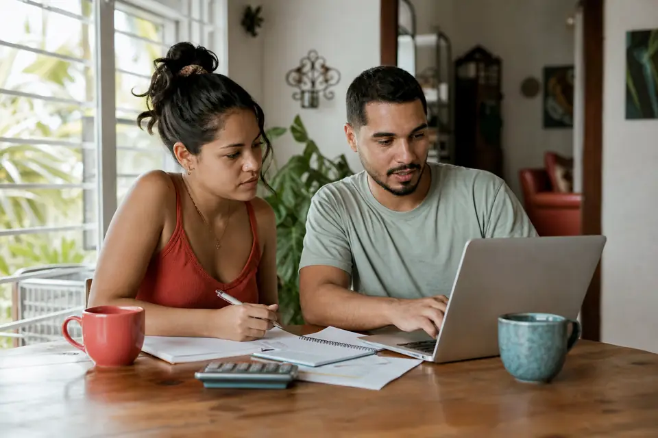 Pareja joven revisando su presupuesto mensual en una computadora portátil en casa.